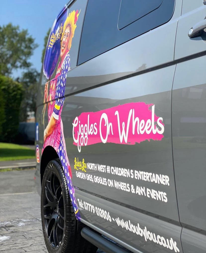 An image of Louby Lou’s transport van with a decal reading “Giggles on wheels; Louby Lou - North West #1 Children’s Entertainer - Garden gigs, giggles on wheels and any events”.