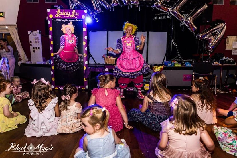 This is an image showing Louby Lou the female clown performing an interactive clown performance complete with comedy and magic for kids at a fun party event. She is dancing for the children in her clown attire.
