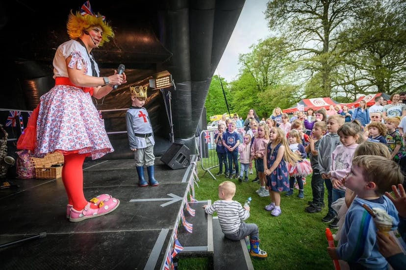 An image of Louby Lou, the clown, on top of a stage, performing to a large crowd of children. There's plenty of giggles on display, from both Louby Lou and the Children. This image was taken in Greater Manchester